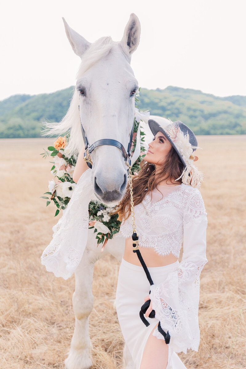 Woman in a white outfit standing next to a large white horse.