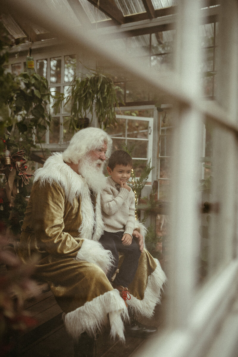 A little boy sitting on Santa's lap to tell him his Christmas wishes.