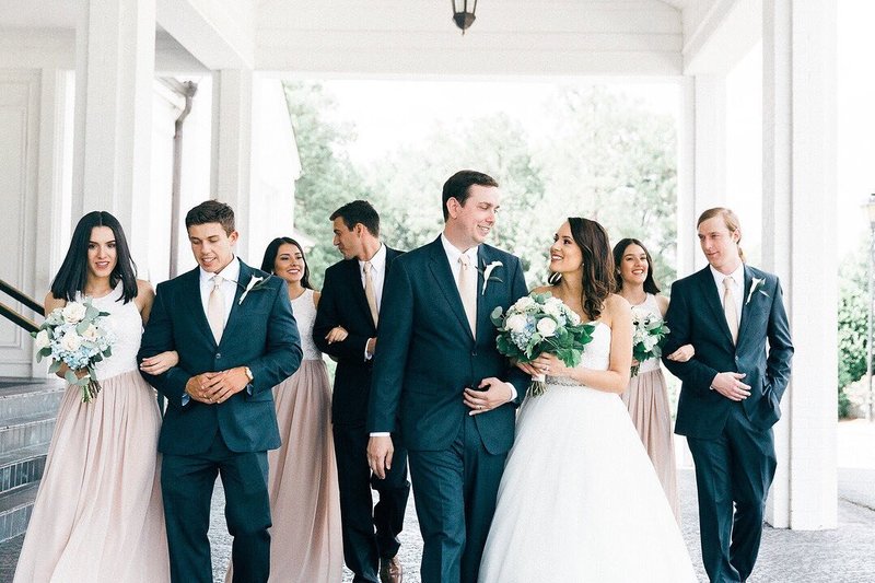 A bride and groom walking and smiling at each other ahead of the rest of their bridal party.