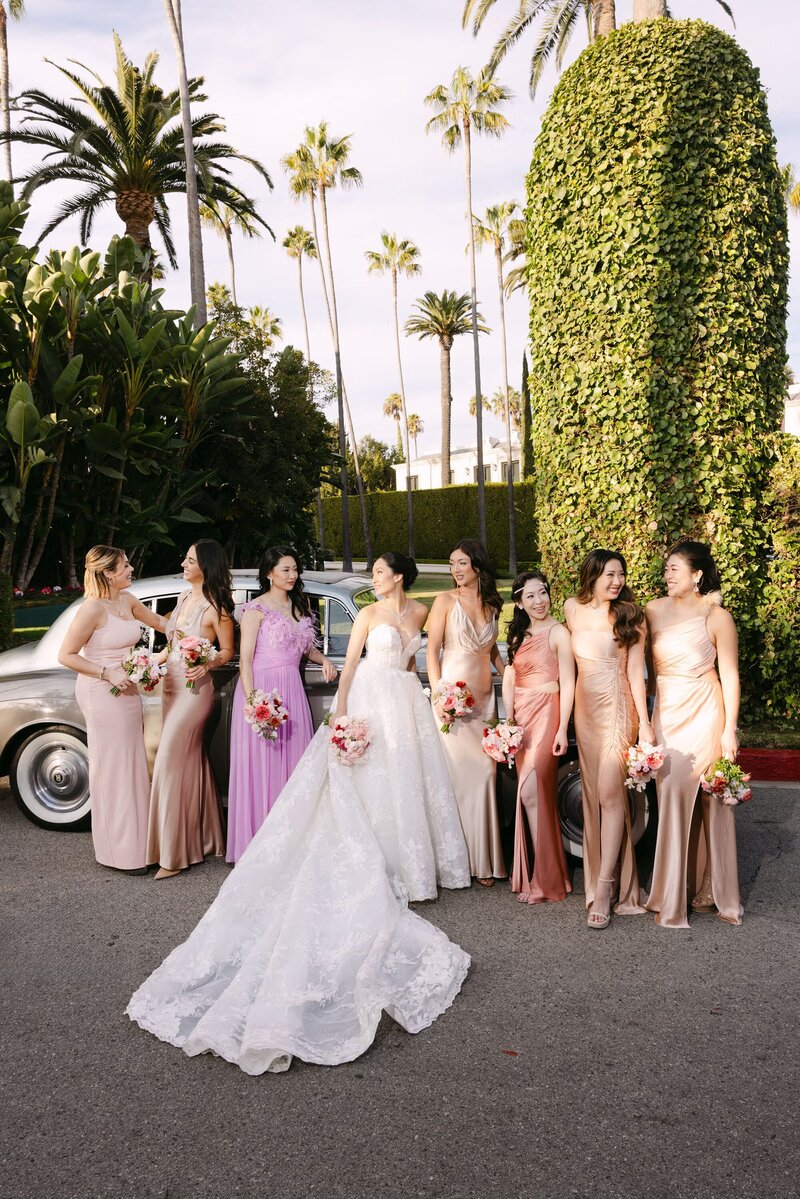 Kohnur bride with soft glam makeup and loose waves wearing a sheer gown and gold floral headpiece in an indoor studio with pink backdrop In Yorba Linda, California.