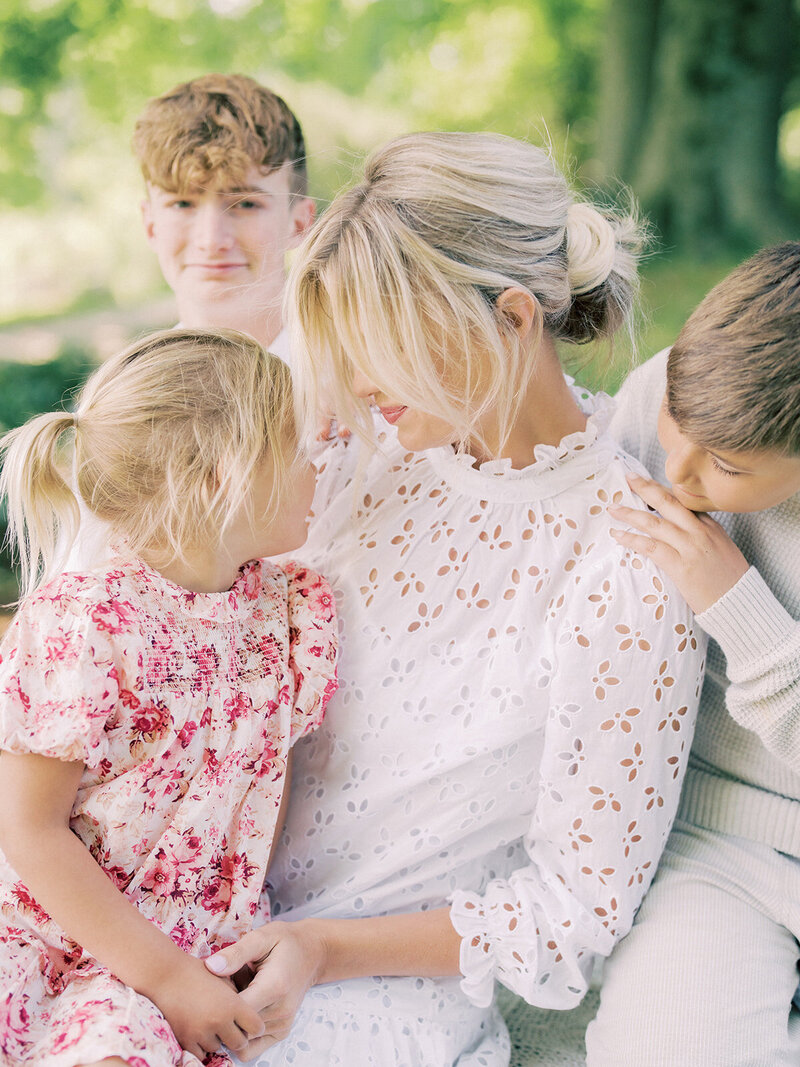 Blonde mother in white dress leans into daughter in pink floral dress surrounded by her sons photographed by Washington DC Family Photographer Marie Elizabeth Photography