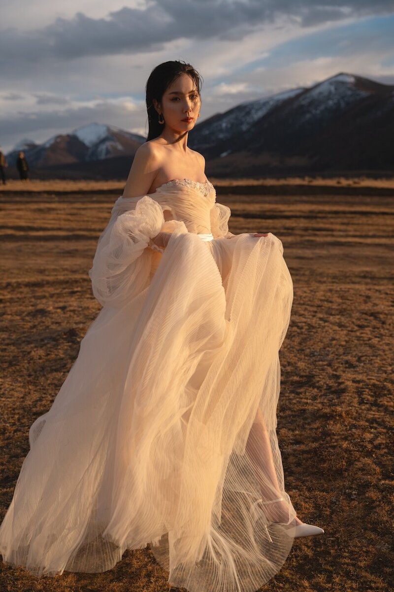 Couture dress bridal shoot on a field with mountains in the background and golden light.