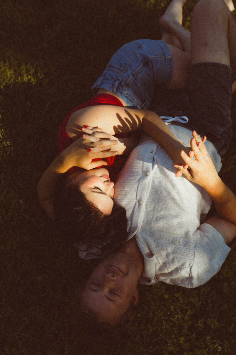 Girl wearing a red shirt snuggling with her boyfriend in the grass during a couples photo session in Columbia, MO.