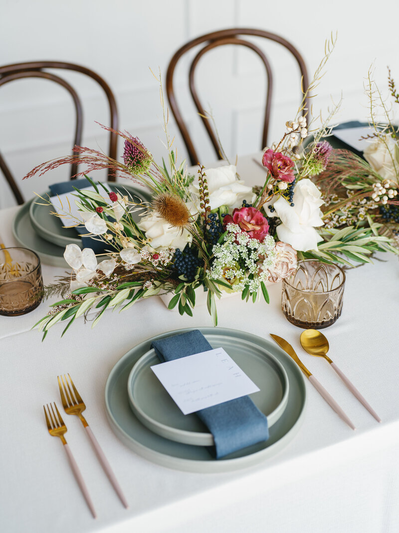 Elegant wedding place setting with custom printed menu, neutral napkin, and white floral centerpiece on a navy linen. 