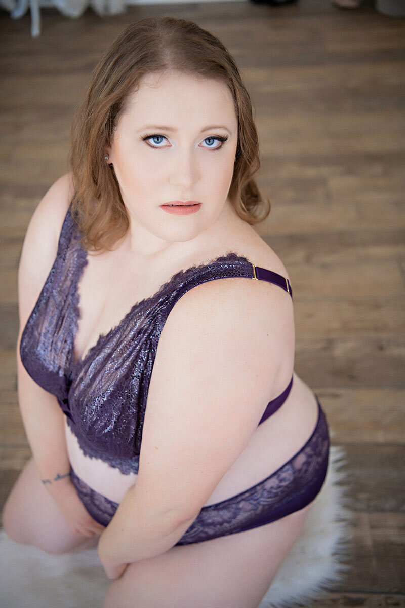 Redhead woman with tattoos poses in edgy boudoir photoshoot.