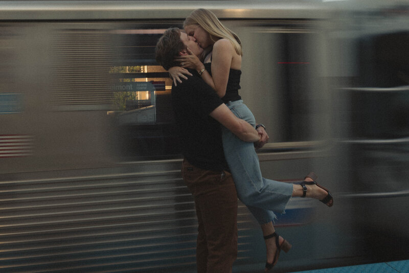 Dramatic, romantic image of a couple sharing a passionate kiss at a train station, with the motion blur of the train symbolizing the rush and excitement of love