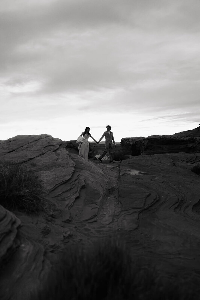 Bride and groom walk hand in hand across canyon cliff in destination wedding