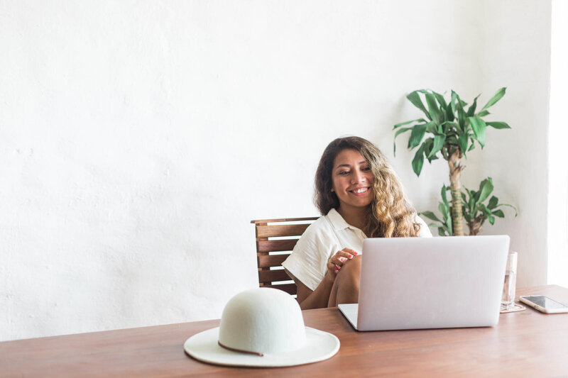 A woman sitting at a table with her laptop smiling. 