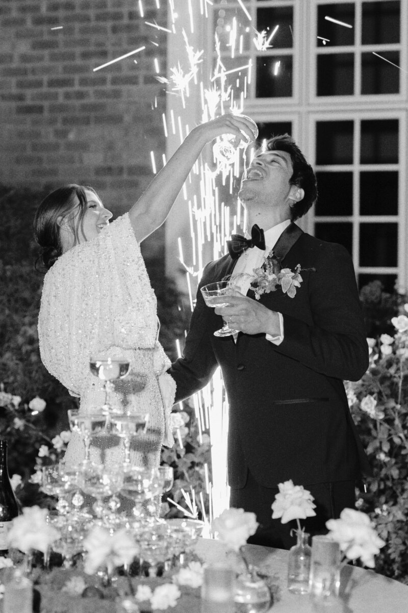bride pouring champagne into grooms mouth with sparklers in the background