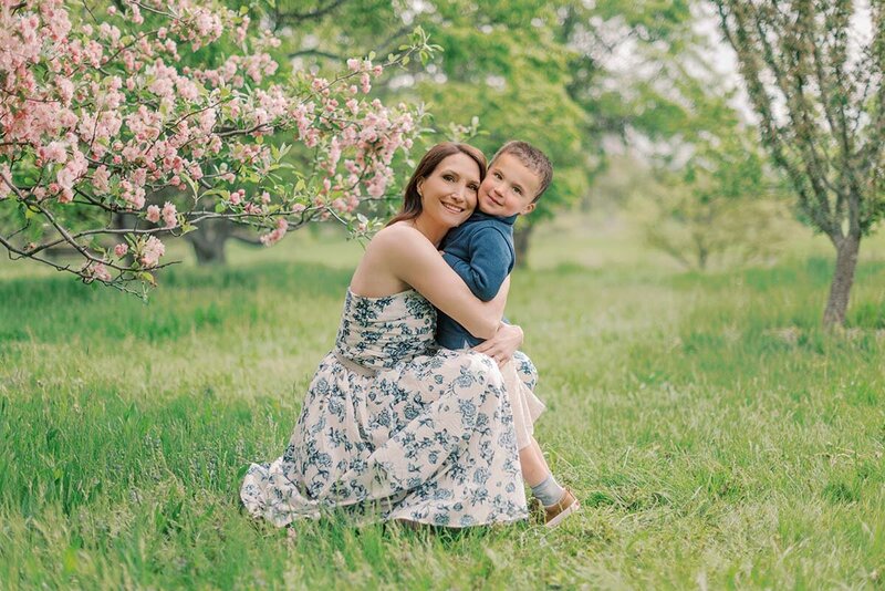 Mother in white floral dress hugging her young son next to a pink flowering tree for her Chicago family pictures