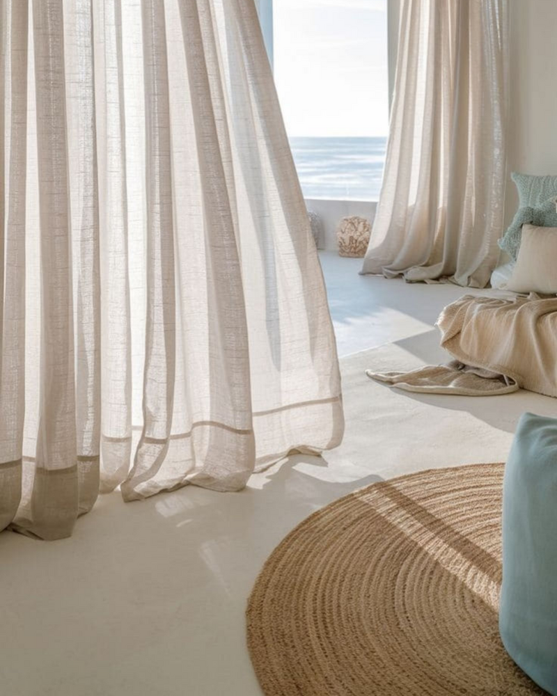Sheer curtains blowing in the breeze beside a cozy corner with pillows, a rug, and an ocean view