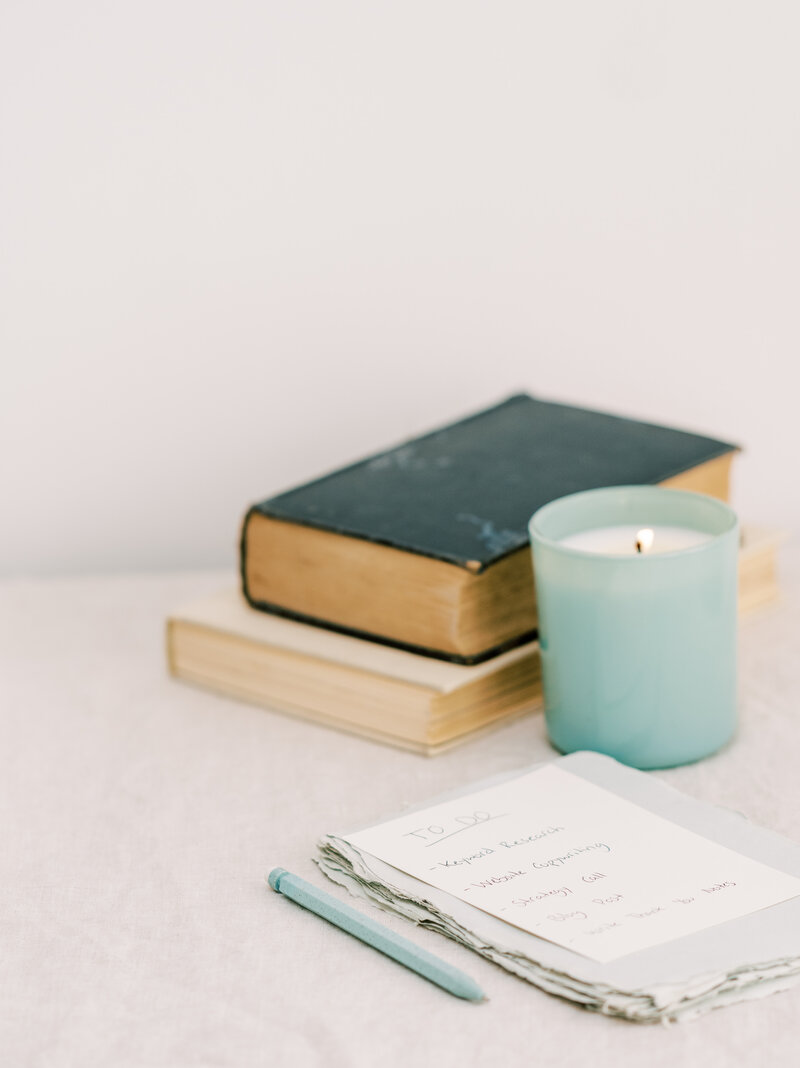 A to-do list for an SEO copywriter on white paper, next to a faded blue candle and a stack of two books