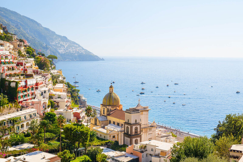Scenic view of Positano on Italy’s Amalfi Coast, showing colorful hillside buildings, the dome of the Church of Santa Maria Assunta, and boats scattered across the blue sea.