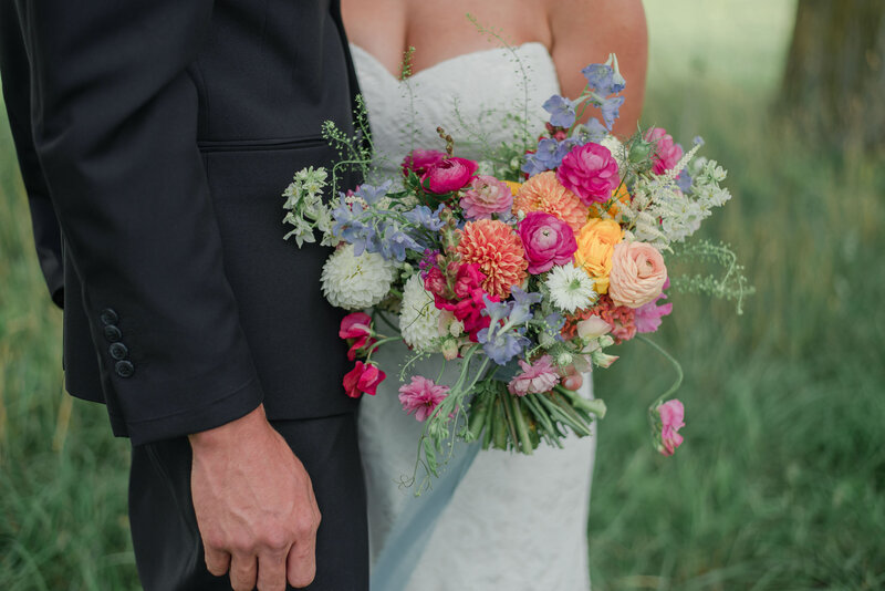 Bride holding a whimsical bridal bouquet featuring dahlias, ranunculus, sweet peas and more.