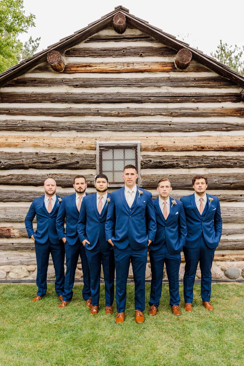 Groomsmen and groom standing outside of a log cabin in blue suits with brown shoes.  Wedding Photographer Milwaukee Wisconsin.