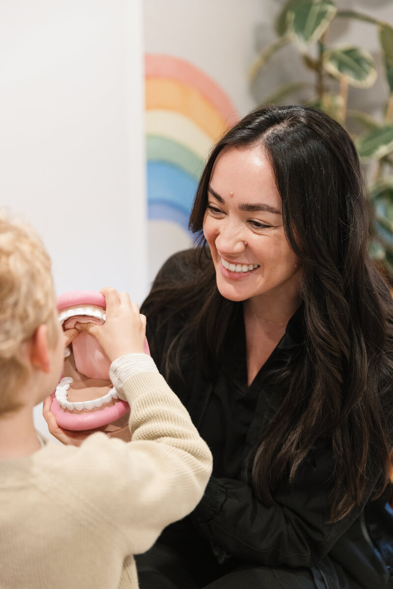 Orofacial Myofunctional Therapist smiling while reviewing a model of the mouth with a young patient.