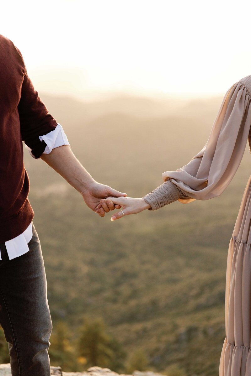 Couple walks romantically hand in hand on cliffside.