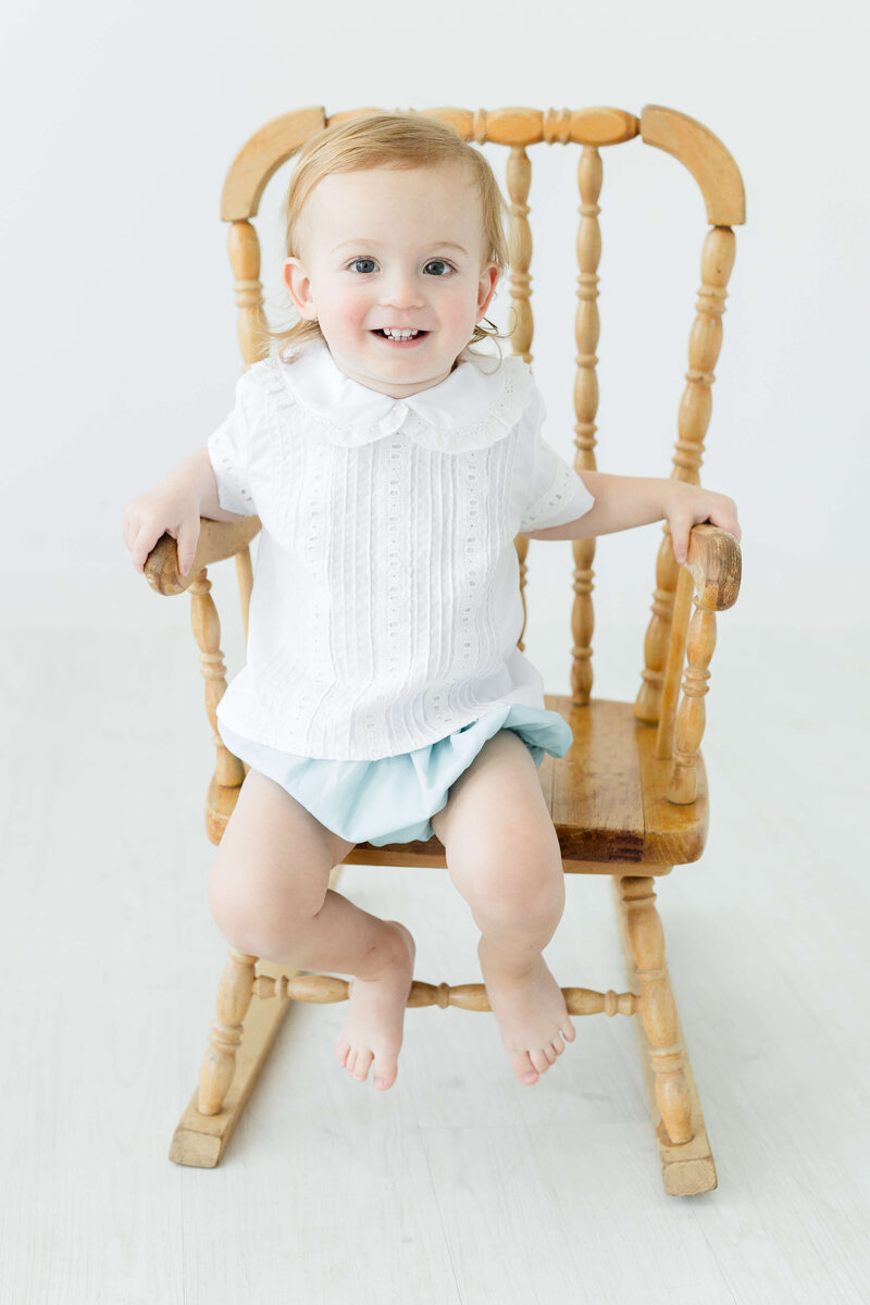 Toddler sitting in chair smiling at camera for milestone photography in mini model rep program