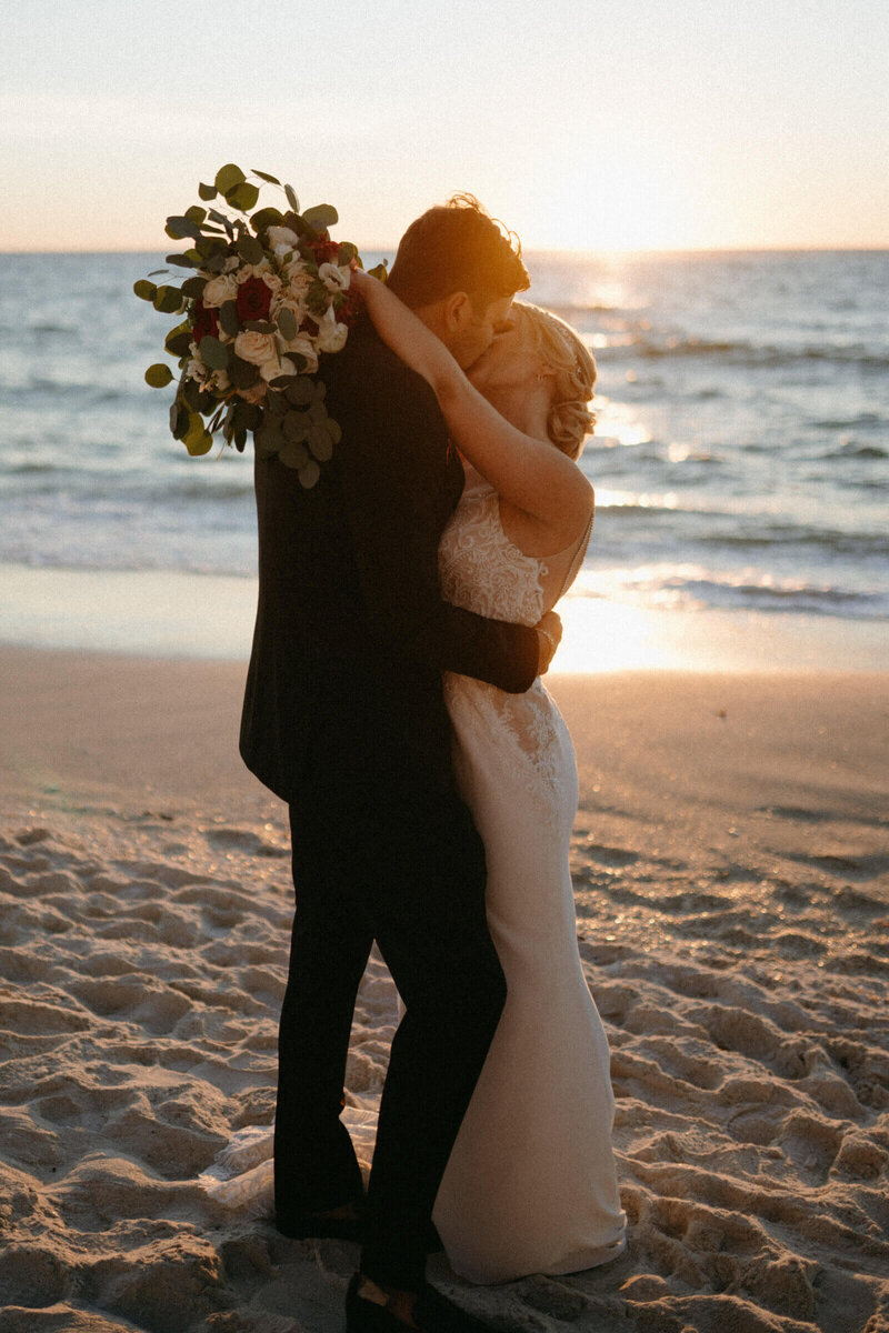 bride and groom kissing and holding bouquet during golden hour by south florida wedding photography