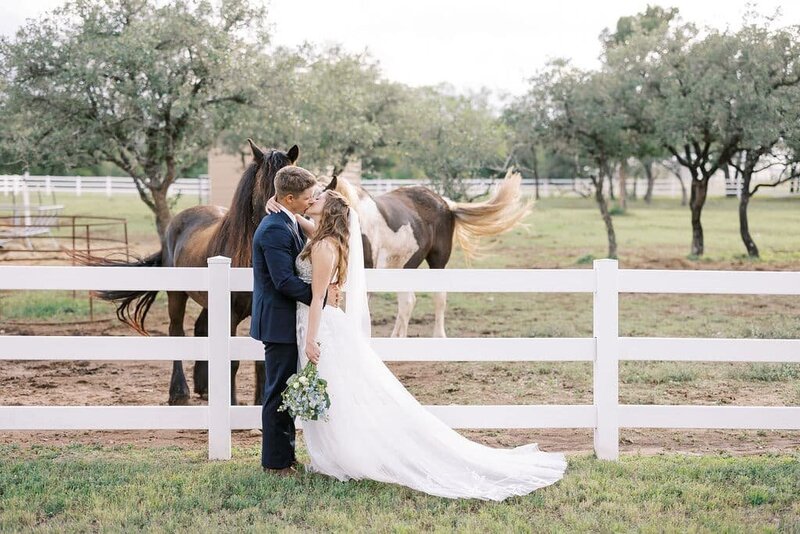 bride and groom kiss in front of horses at ranch