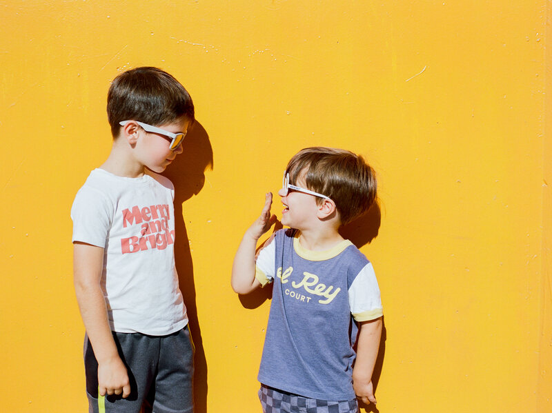 film photograph of two young brothers standing against a bright orange wall