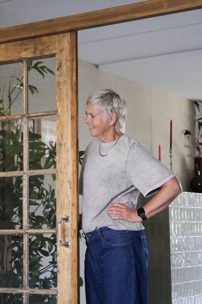 Threa van LOOSZ Interieur & Styling staat naast rustieke houten ensuite deuren, met een moderne mix van texturen en materialen op de achtergrond