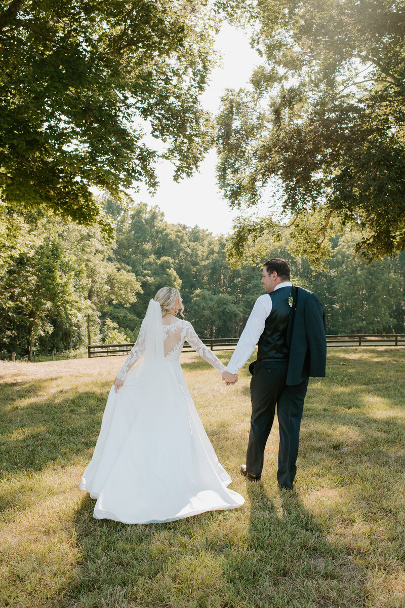 Bride looking back at the camera as she holds hands with her groom and walks into the sunset during their summer Richmond wedding