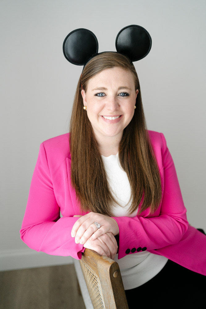 Pinks & Greens Travel Co. Founder Rachel Salley looks directly at camera and smiles while wearing a pink blazer and classic black Mickey Mouse ears.