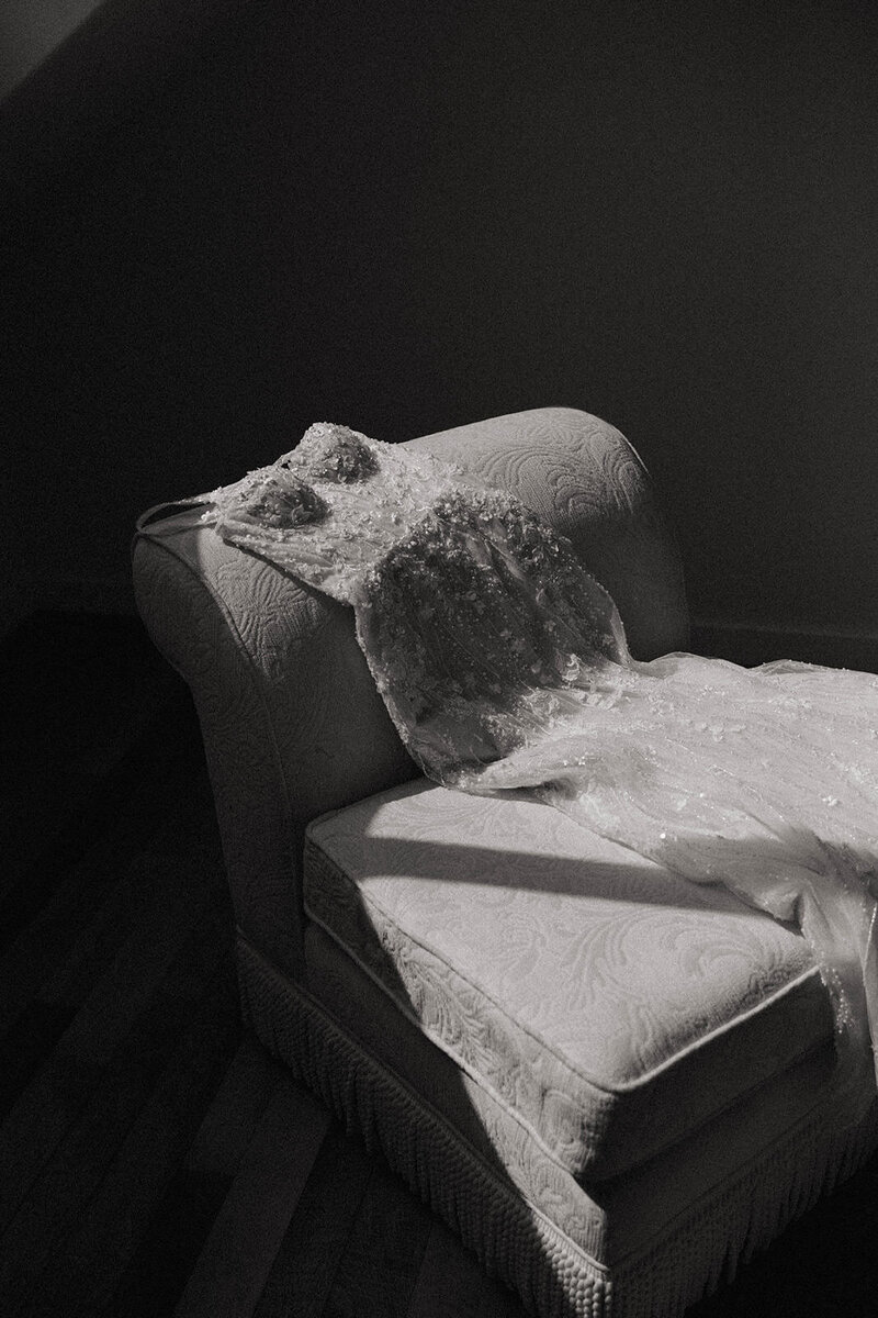 Bridal gown with intricate beading draped over a vintage chair in soft window light, photographed by a Washington wedding photographer.