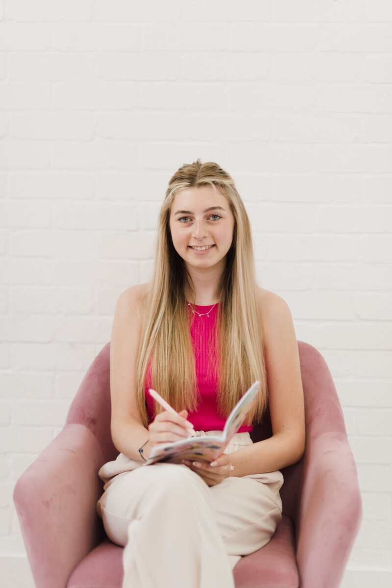 Katie of Plymouth Marketing Agency Established by her sat in a chair holding a notebook and a pen