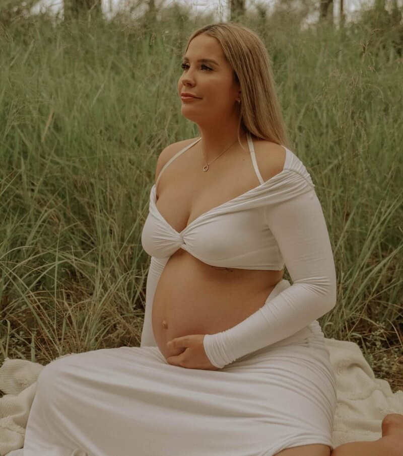 Pregnant woman sitting in a field holding her stomach