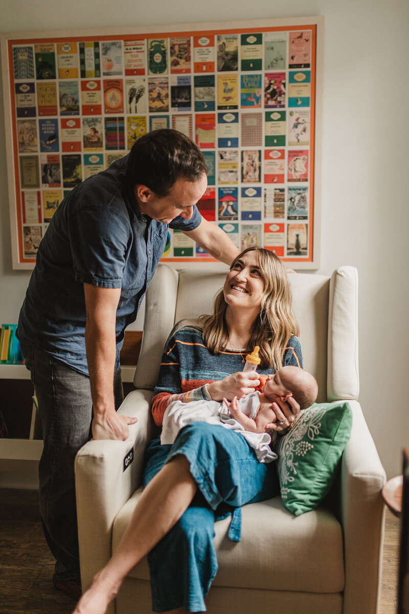 mom  bottle feeds her newborn in her nursery while dad looks on lovingly  in their historic Phoenix home