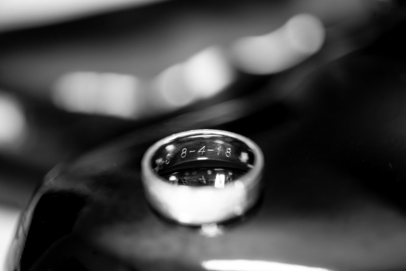 A black and white picture of a groom's wedding band on the end of his black shoe
