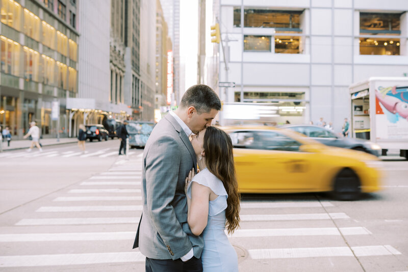 Engaged couple in midtown Manhattan in front of a taxi zooming down the street.