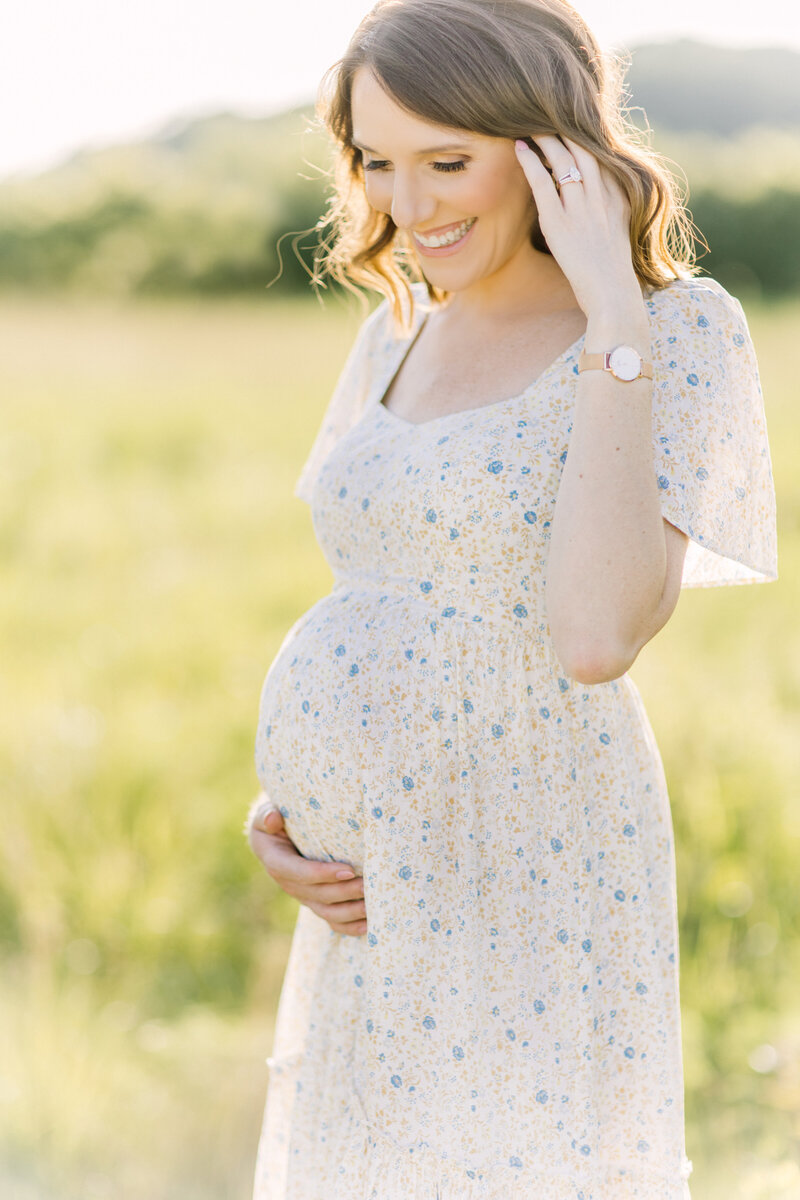 Mom in a light blue floral dress holding her baby bump for her maternity photos by Kansas City maternity photographer Jeanna Hayes