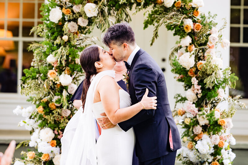 Wedding couples first kiss surrounded by a colorful floral arch in Toledo Ohio