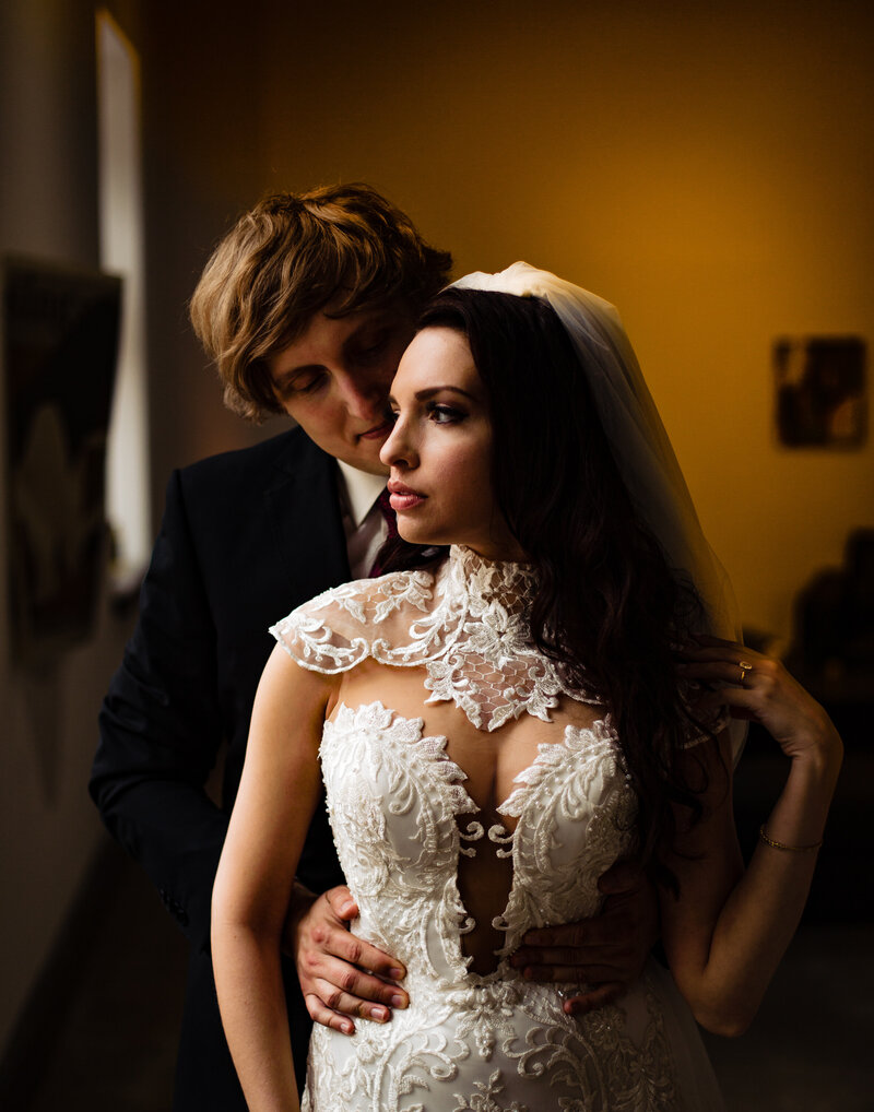 A wedding couple embracing in front of a window at Registry Bistro in Toledo Ohio. The bride is wearing a very modern dress with a collar