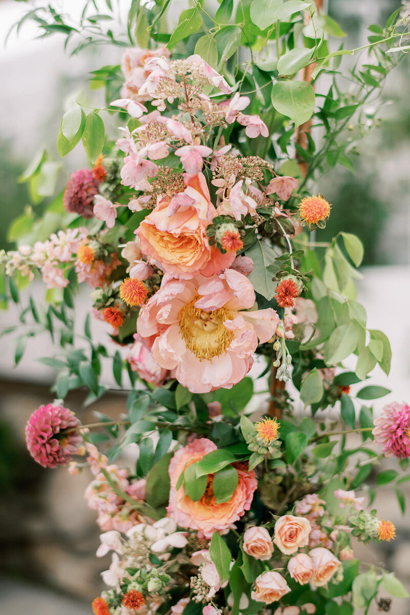 Closeup of creative floral wedding detail with pink, peach, and yellow flowers accented with green botanicals at Catskills wedding
