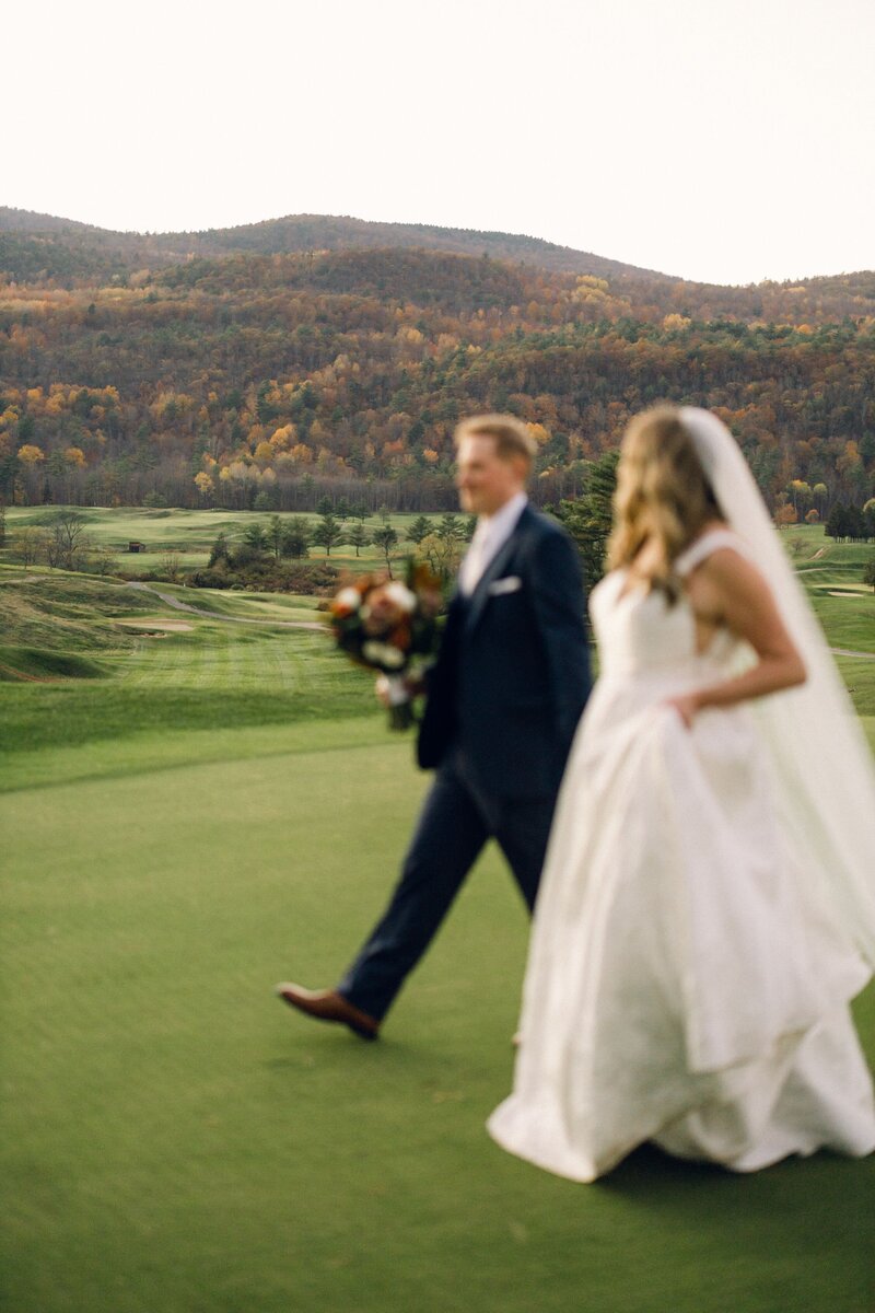 A bride and groom walk together across the Ticonderoga Golf Course after their wedding ceremony.
