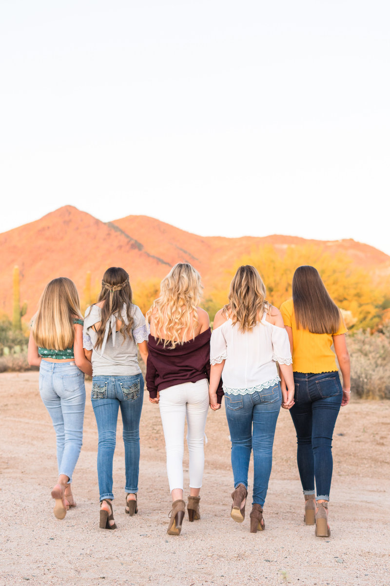 Five girls walking holding hands at sunset in the desert