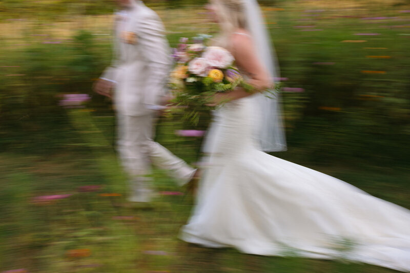 Warm motion-blur image of bride and groom walking through flower fields at Long Hollow Garden wedding