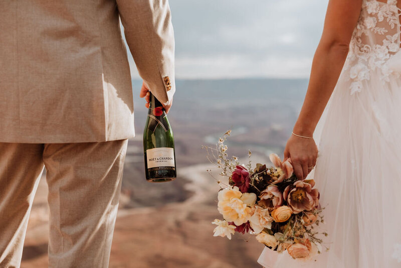 bride and groom holding champagne and bouquet in the desert