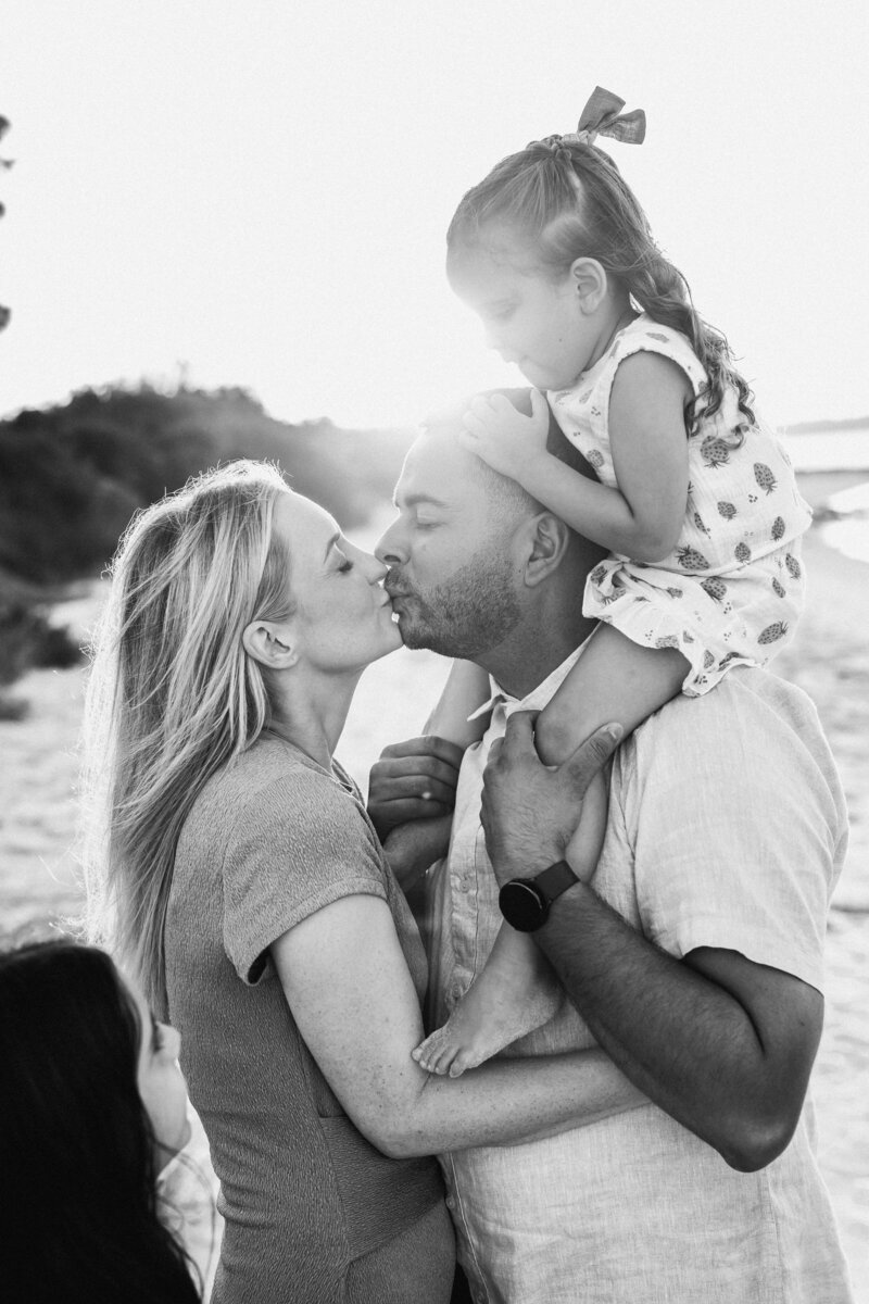 Parents kissing while surrounded by three young children during family beach photoshoot in Sydney