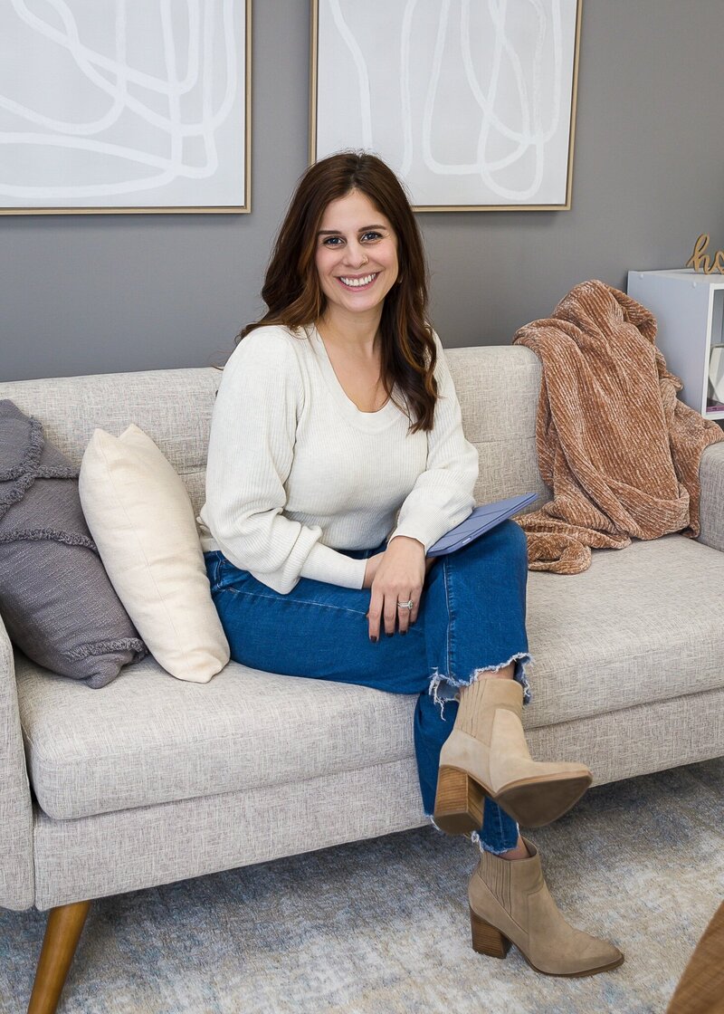 Woman with brown hair sitting on couch in a living room smiling
