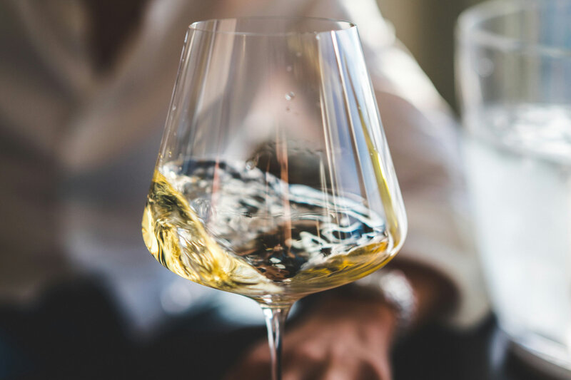 Close-up of a person swirling white wine in a clear wine glass, causing the liquid to splash and create patterns on the glass
