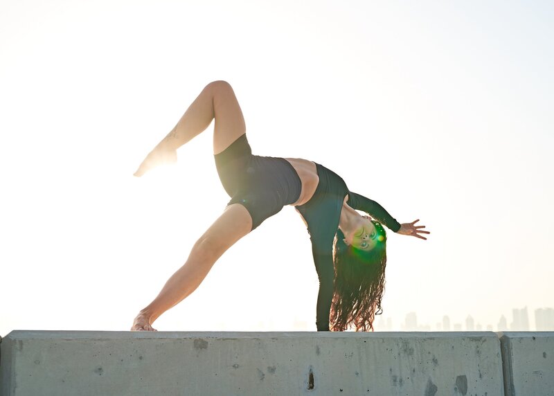 Sarah performs an inverted yoga pose against a bright sky with the city skyline in the backdrop.