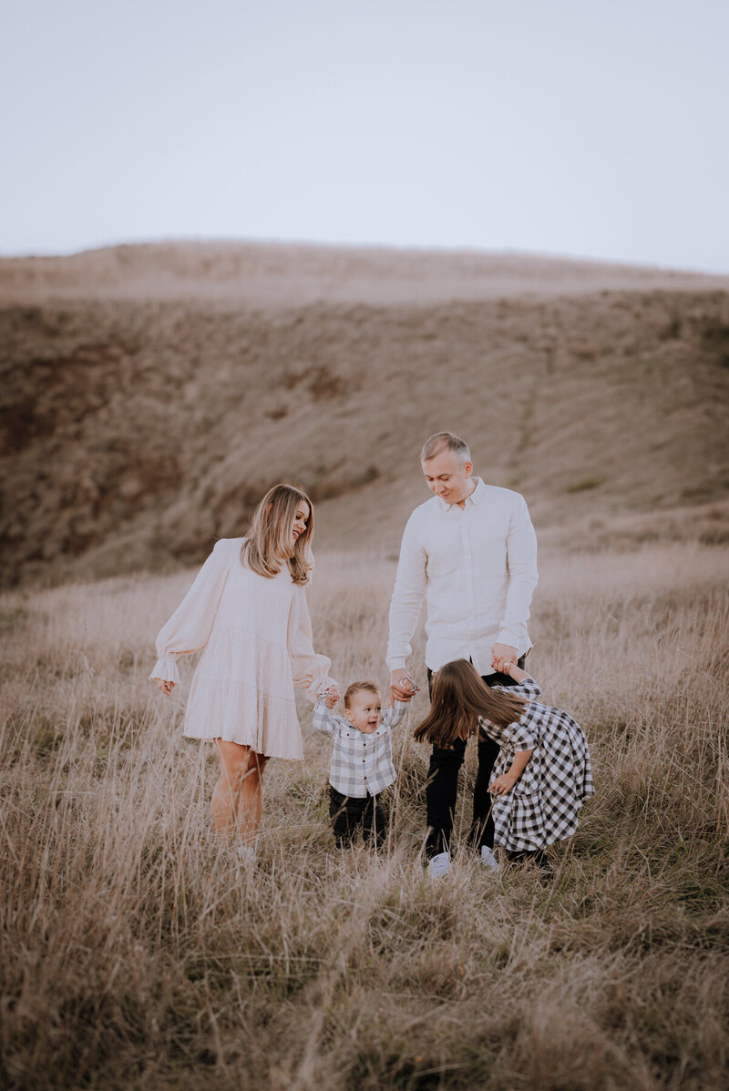 Family of four walking through a grassy field holding hands
