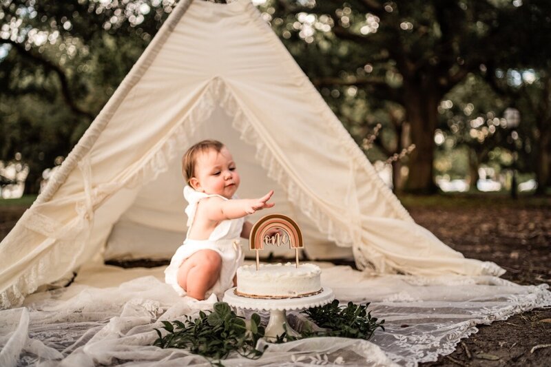 Smiling baby sitting in a cozy outdoor tent during a one-year milestone session