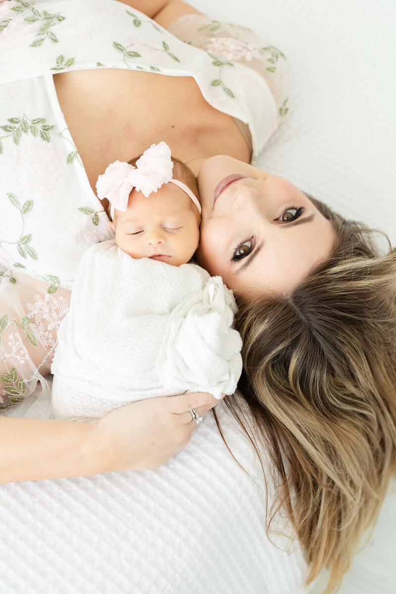 Mom and baby laying down heads next to eachother while mom is smiling at the camera during newborn photogrpahy session