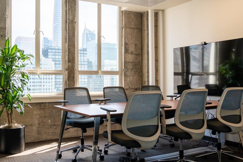 Contemporary office with glass meeting pods, green divider planters, and bright natural light.